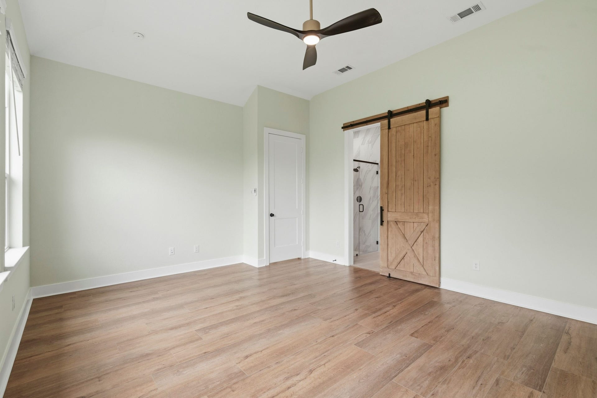 The Primary Bedroom offers exceptional space and versatility, easily accommodating a king-sized bed, matching nightstands, a dresser, and a dedicated media area. A tranquil Retreat with ample room to create your ideal sanctuary. Its finished with a designer black and champagne gold ceiling fan and a custom barn door offering seamless access to the luxurious Bath