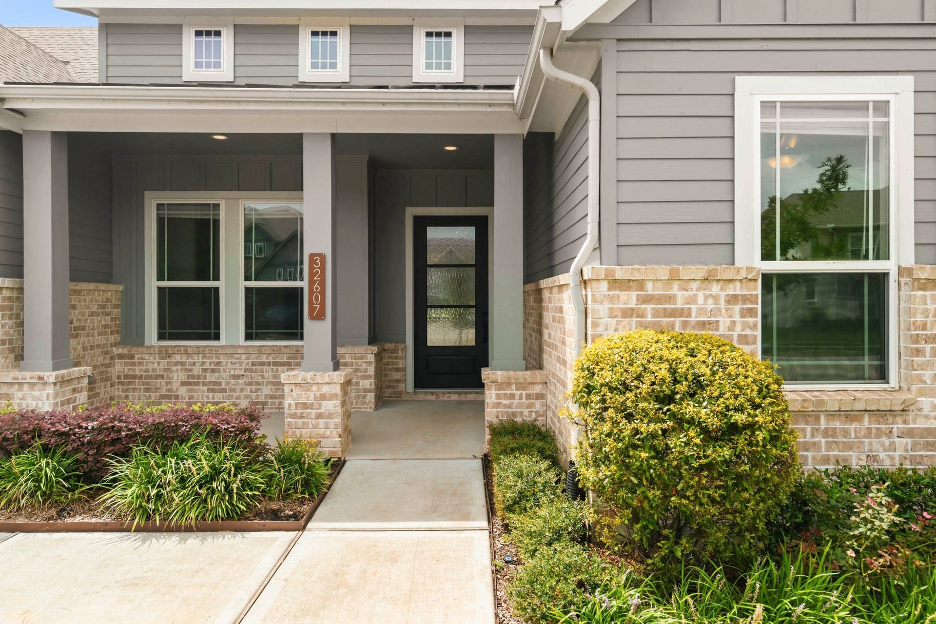 Guests are welcomed by a spacious covered Front Porch, highlighted by stately brick-anchored columns, elegant recessed lighting, and a sleek rain glass front door. A beautifully landscaped walkway guides visitors to the entrance, framed by professional landscaping. Even better? The front yard is maintained by the HOA!