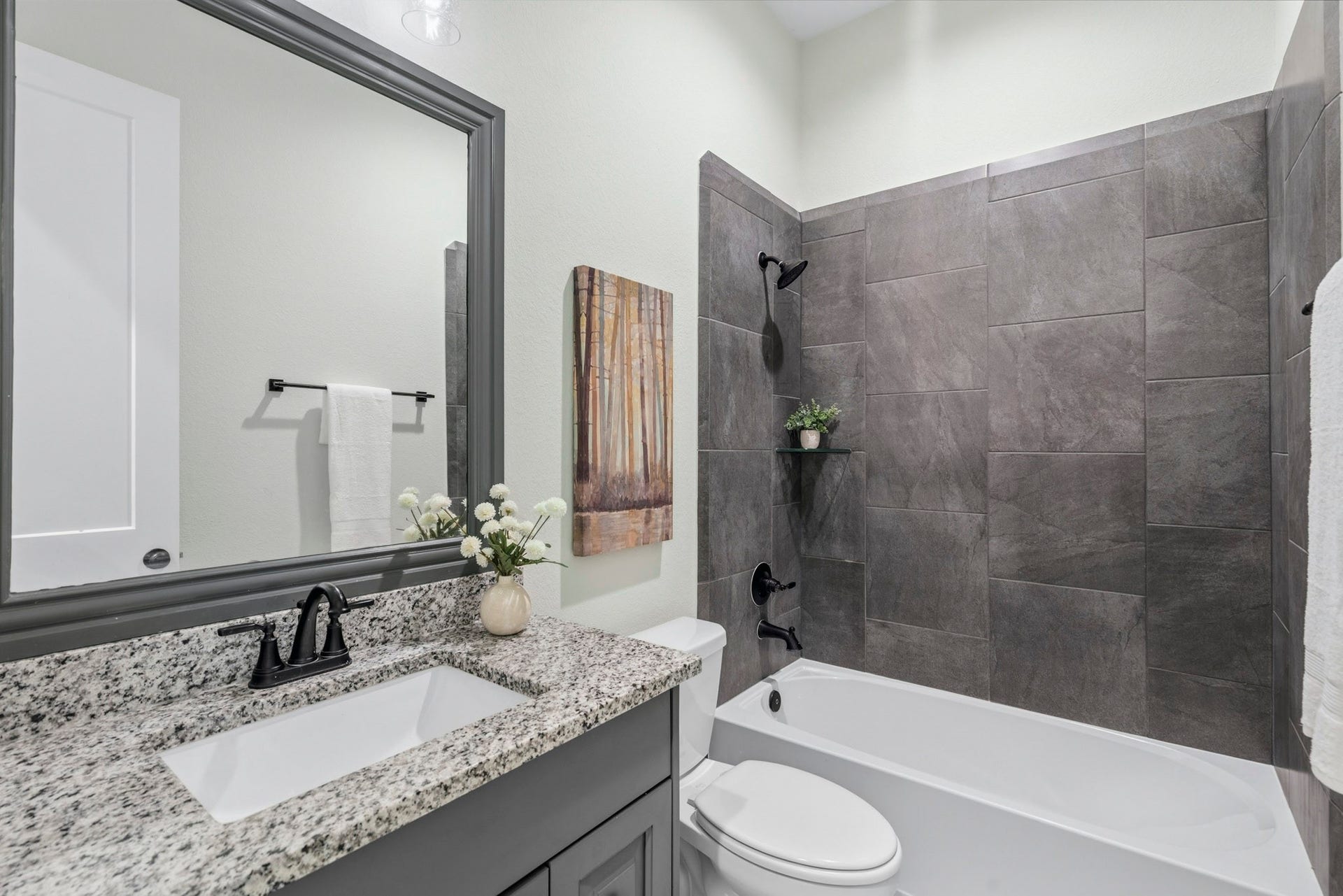 This is a view of the full Bath that serves two Secondary Bedrooms. It is beautifully appointed, featuring a vanity with an undermount sink, granite countertops, and a customed framed mirror that adds another stylish touch. The shower/tub combination also offers a designer's touch to complete the room.