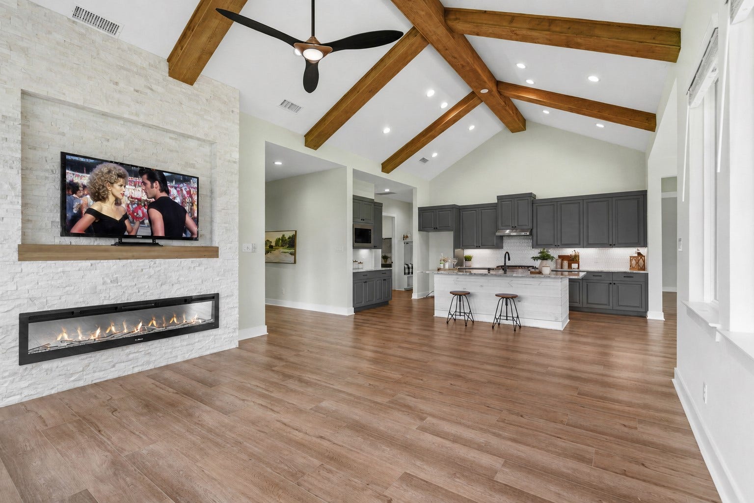 This view of the Family Room better showcases the stone wall, the designer ceiling fan and how the warm, rich tones of the LVP flooring flows effortlessly into the Kitchen, creating a seamless and inviting open-concept living space.