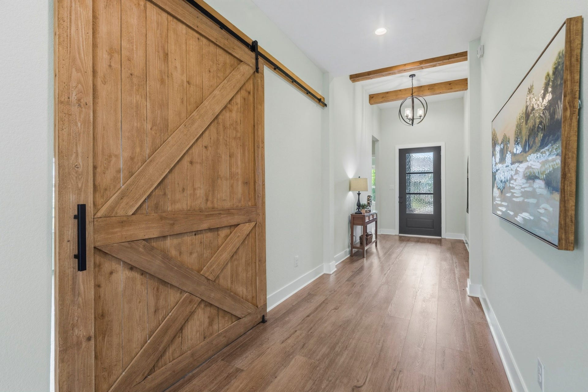 This view of the Foyer captures the striking custom barn door that slides open to the Study and adds warmth and character to the space. An elegant upgraded wrought iron round pendant light illuminates the space. There is also plenty of room for a sofa table or bench seat.