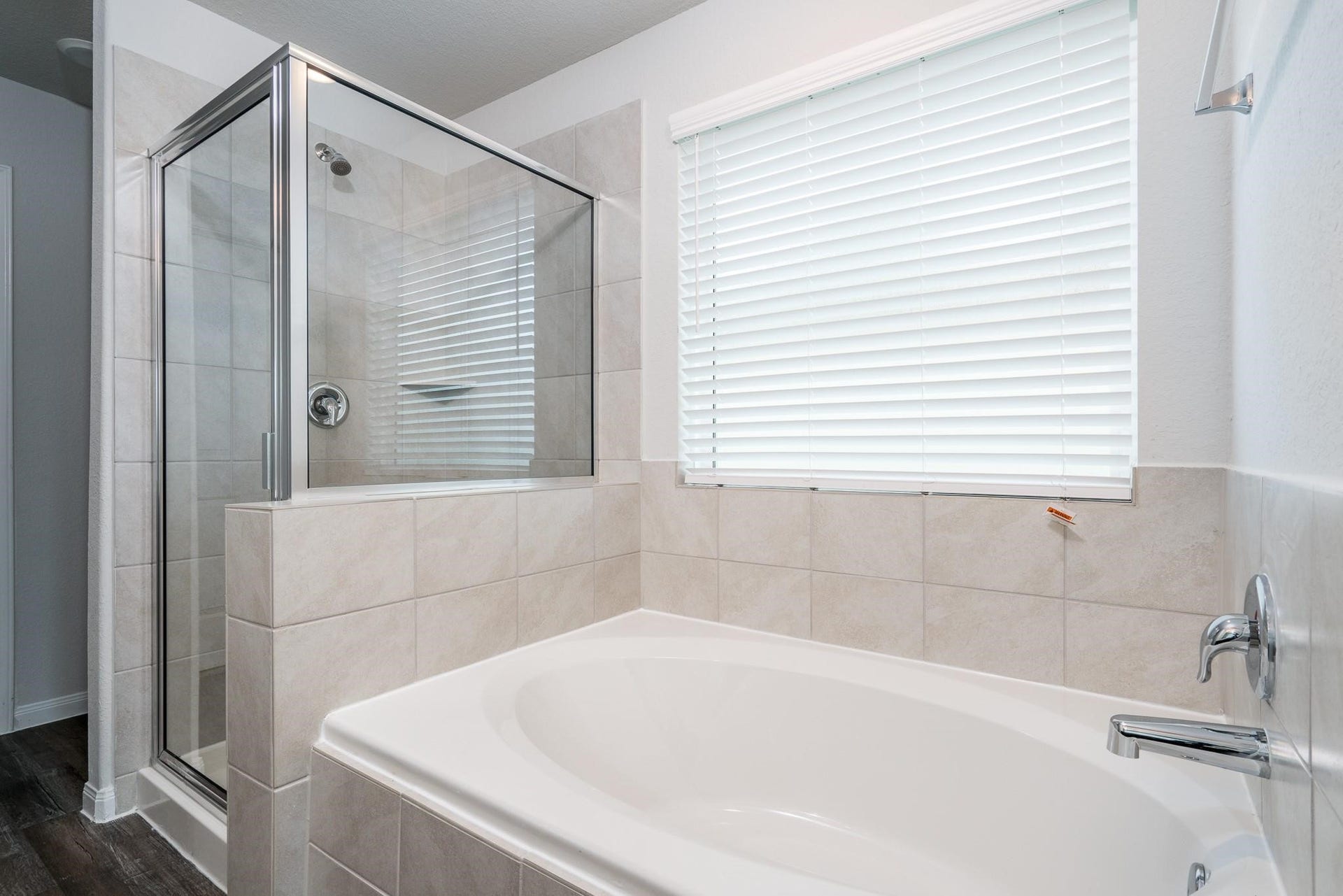 2910 Orchid Ranch Drive, Katy, TX 77494 Bright and inviting bathroom with a large soaking tub and a separate glass-enclosed shower, accented by neutral tile and a window with blinds for privacy.