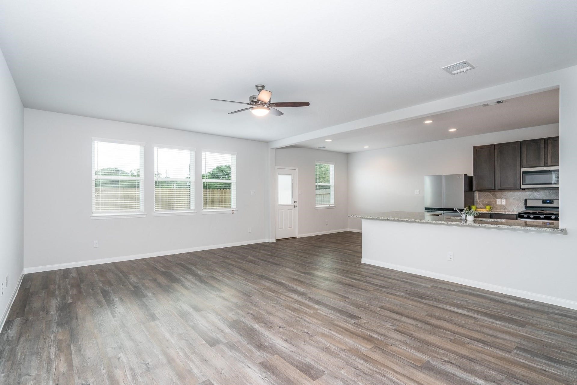 2910 Orchid Ranch Drive, Katy, TX 77494 Spacious open-concept living area with stylish wood flooring, modern ceiling fan, and abundant natural light, seamlessly flowing into a sleek kitchen with stainless steel appliances and granite countertops.