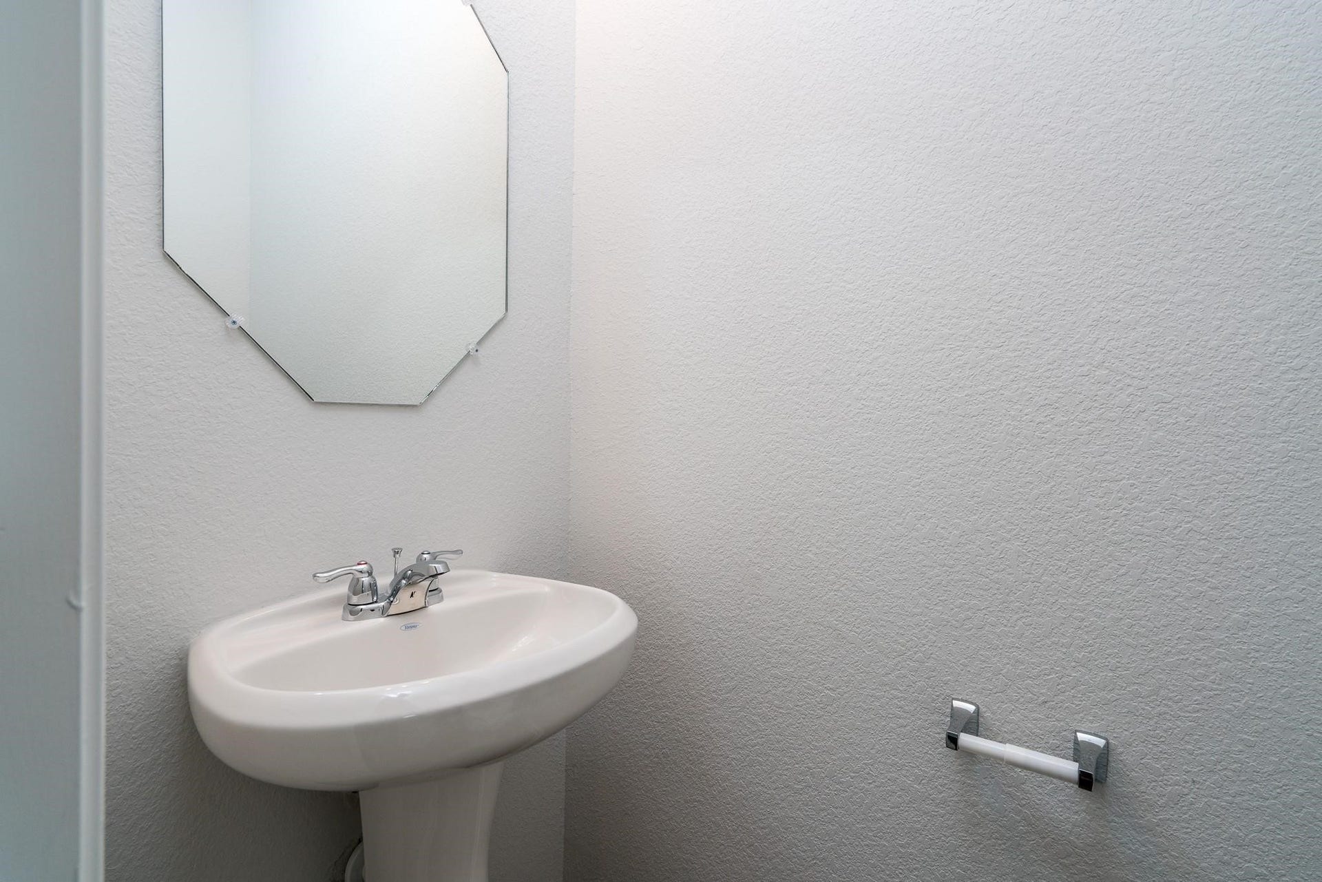 2910 Orchid Ranch Drive, Katy, TX 77494 Cozy half-bath featuring a sleek pedestal sink, angular mirror, and minimalist design perfect for guests.