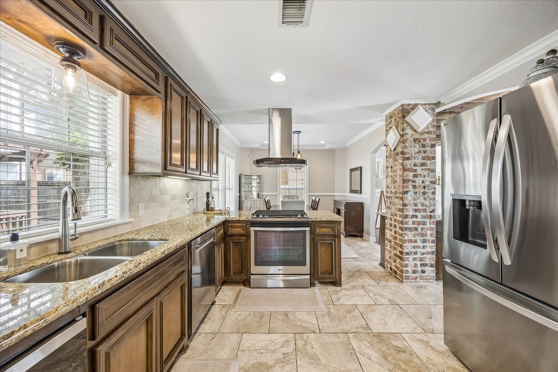 1909 Rosewood Street, Houston, TX 77004 Granite countertops, rich wood cabinetry, stainless appliances, and gas cooking line the kitchen, with a brick column adding texture at the far end.