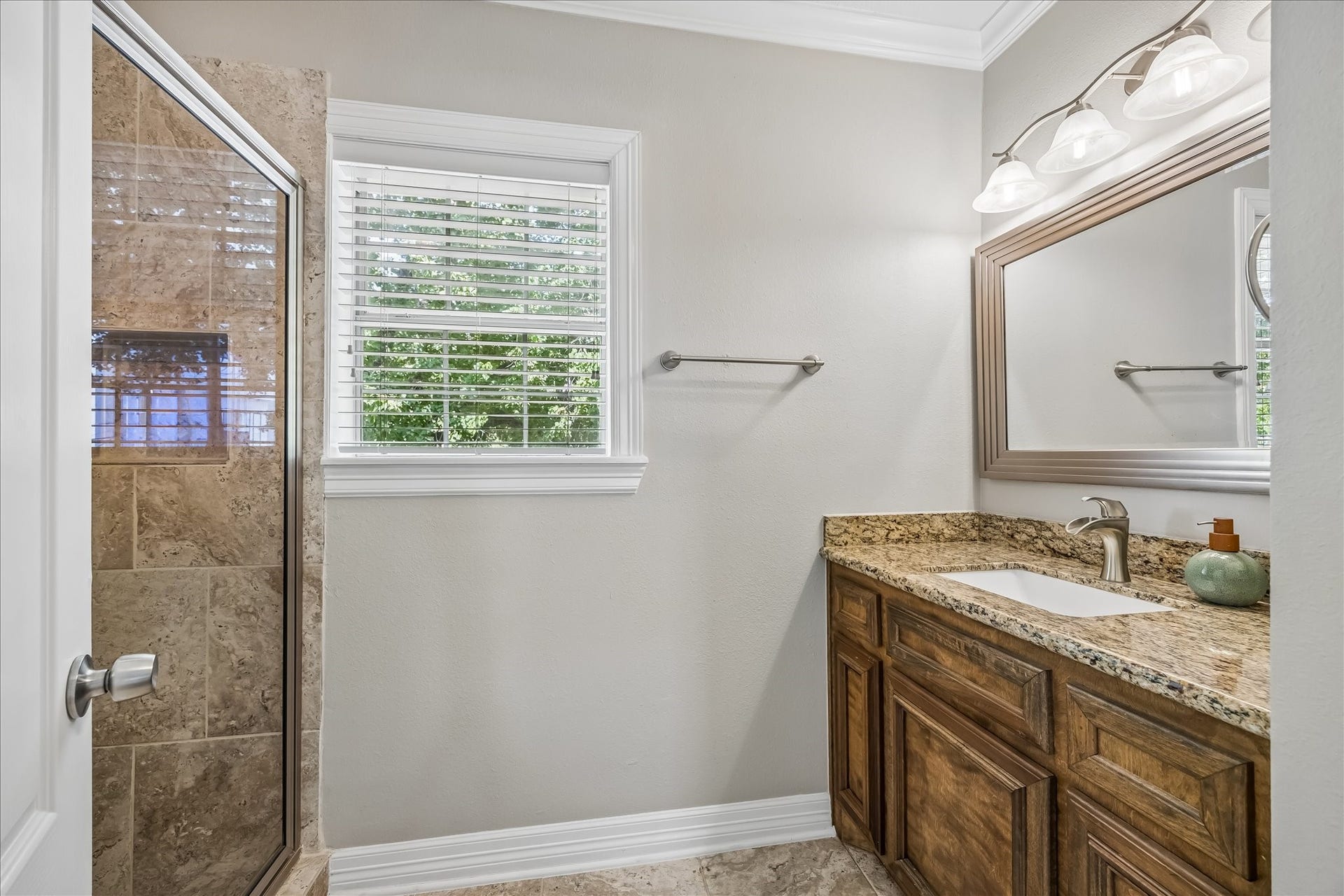 1909 Rosewood Street, Houston, TX 77004 Secondary bath pairs a granite-topped wood vanity with a glass-enclosed stone shower and natural light from the window.