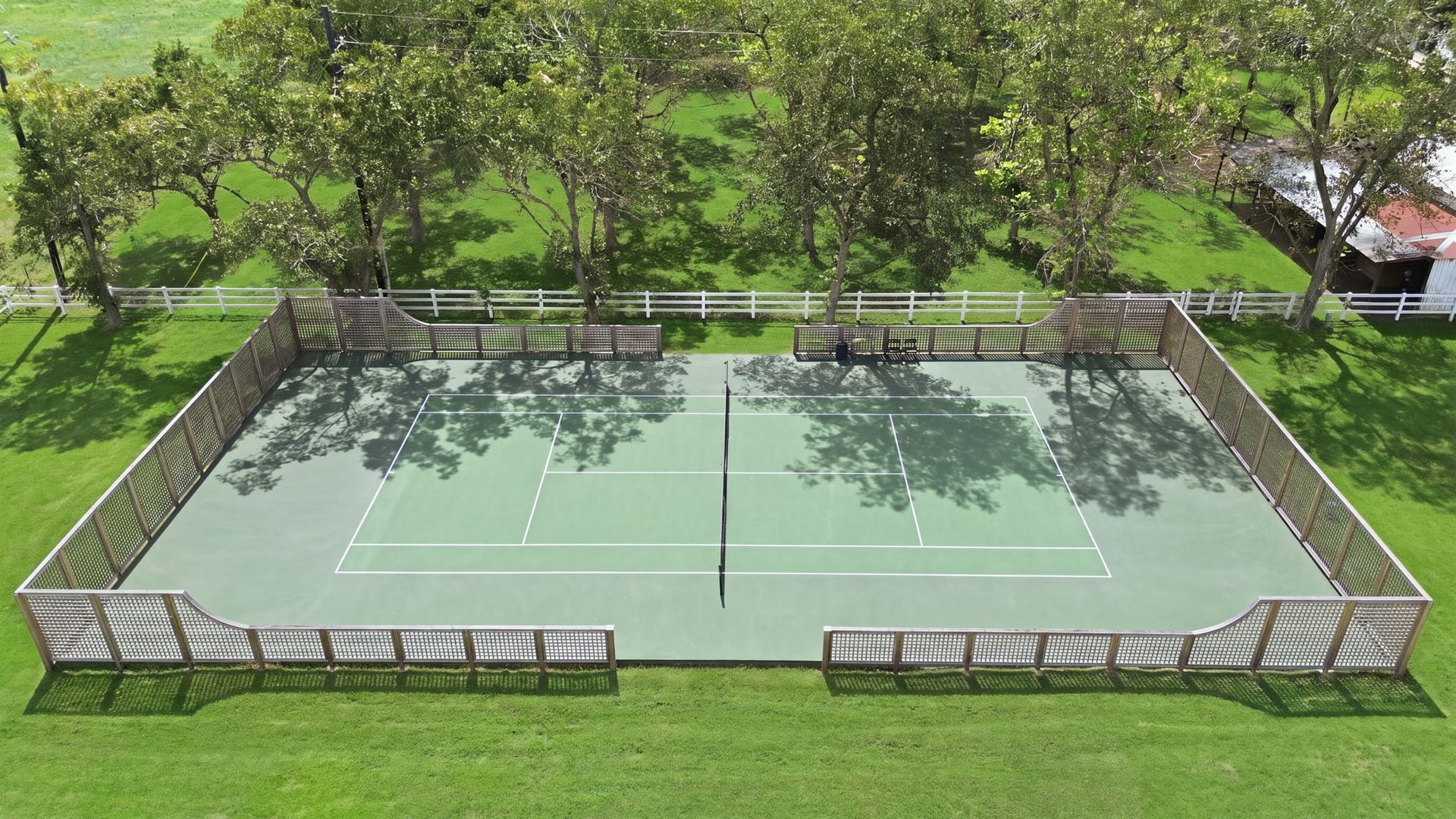 Enjoy your own private tennis court surrounded by lush greenery and a charming lattice fence, perfect for both leisure and serious play.