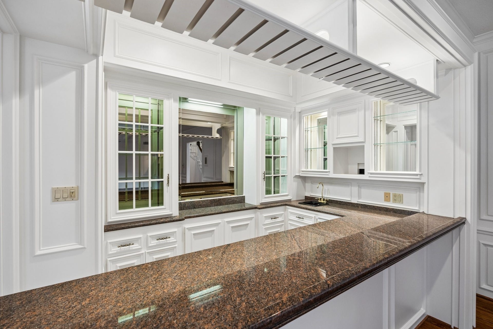 10 Stillforest Street, Piney Point Village, TX 77024 Perfectly positioned to serve the living room, sunroom, and dining room, the custom wet bar features granite countertops, a serving window, mirrored walls, glass shelving, abundant cabinetry, and a built-in TV niche.