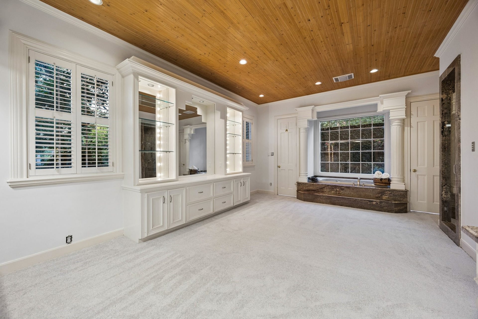 10 Stillforest Street, Piney Point Village, TX 77024 A true spa-inspired retreat, the expansive primary bath features a raised Jacuzzi tub nestled in a sunlit alcove with a window overlooking a secluded brick garden.
