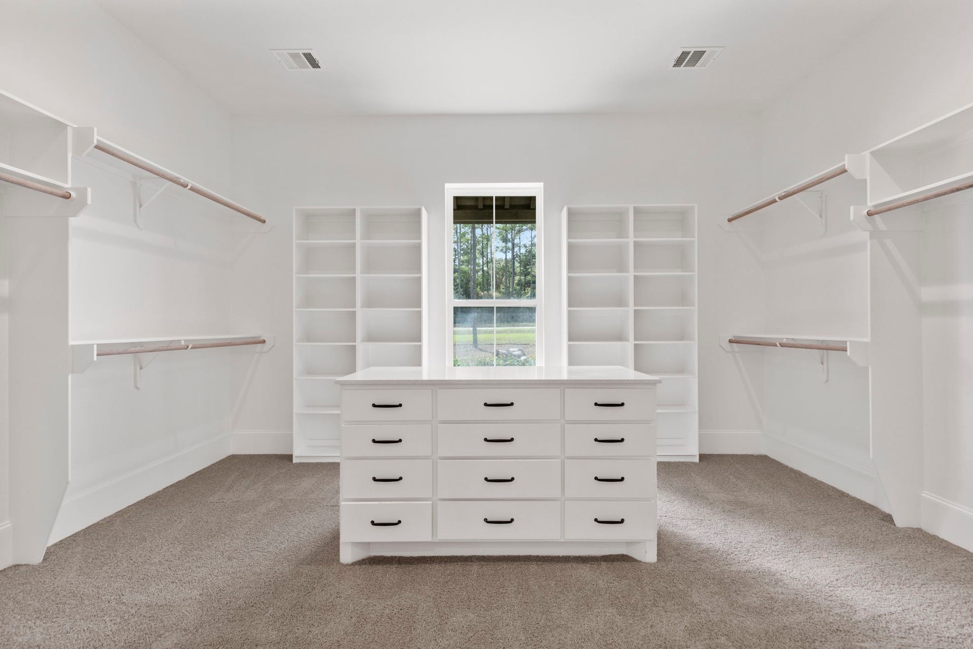 Spacious primary closet featuring custom shelving, generous hanging space, and a central packing island with extensive drawer storage.