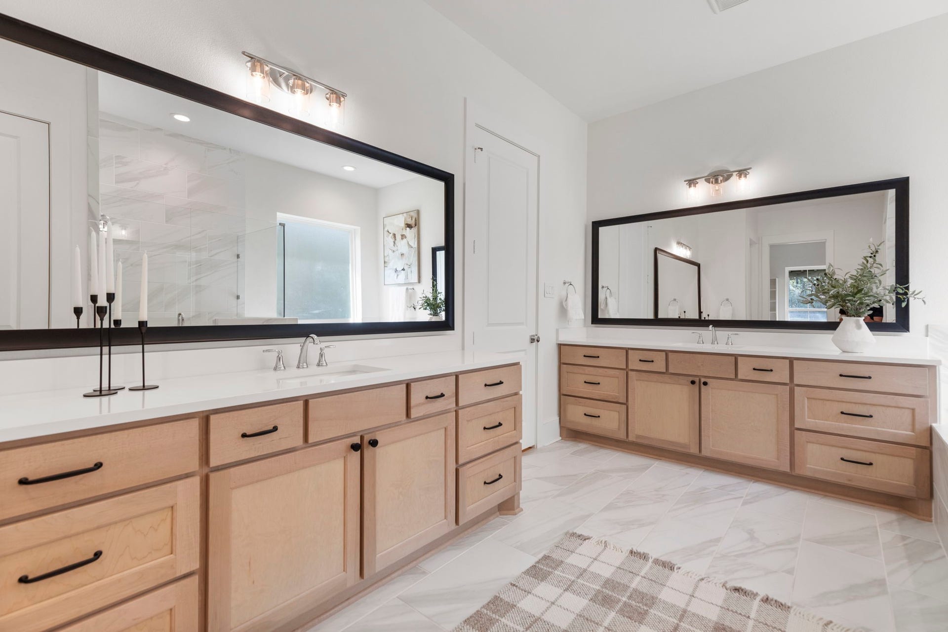 The primary ensuite features modern light wood dual vanities accented by matte black hardware and crisp white quartz countertops, contributing to a fresh, sophisticated aesthetic.