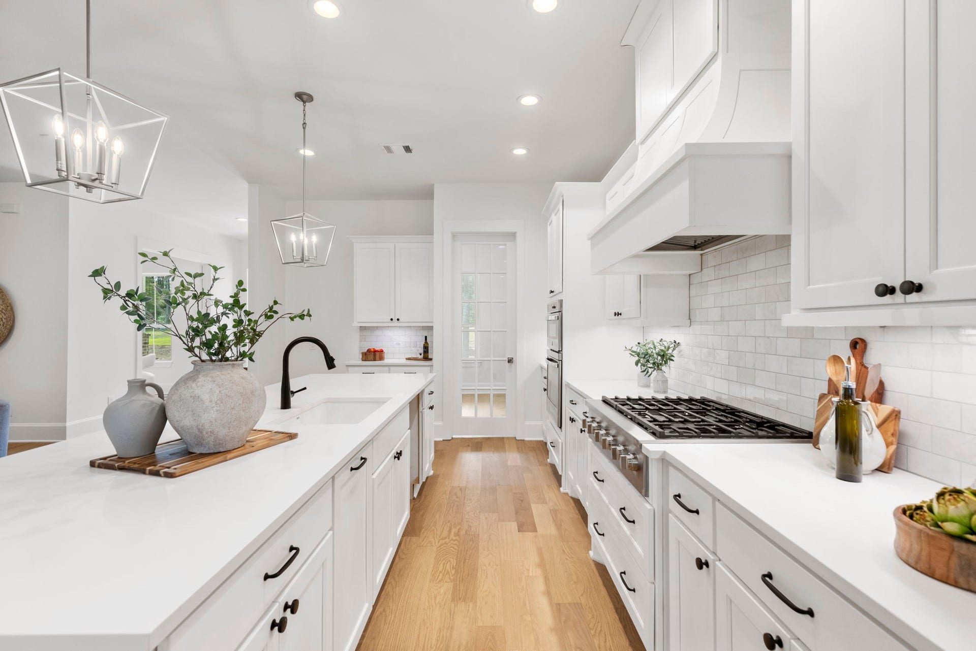 The matte black cabinet hardware provides a modern farmhouse aesthetic that perfectly complements the faucet, while the adjacent glass door opens into a spacious walk-in pantry.
