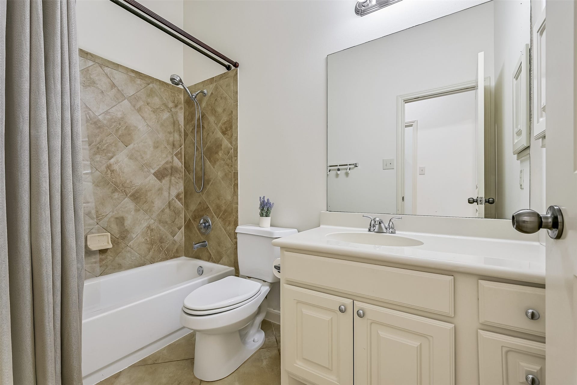 The secondary bathroom features a tub/shower combination with attractive diagonal tile surround, a spacious vanity with white cabinetry & a large mirror. Neutral tile flooring, brushed-nickel fixtures & a convenient location near the secondary bedrooms make this a functional addition to the single-story floor plan.