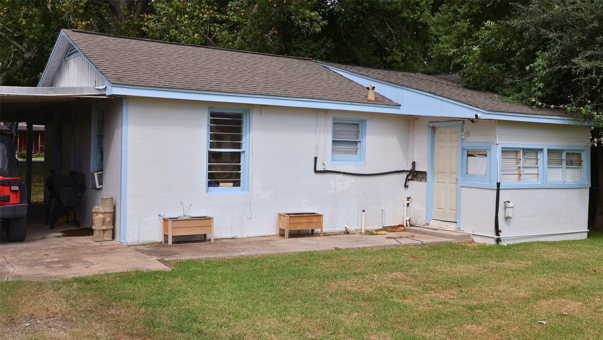 7029 Church Lane, Hitchcock, TX 77563 Cozy single-story home with charming blue trim and a convenient attached carport, nestled in a green, tree-lined yard.