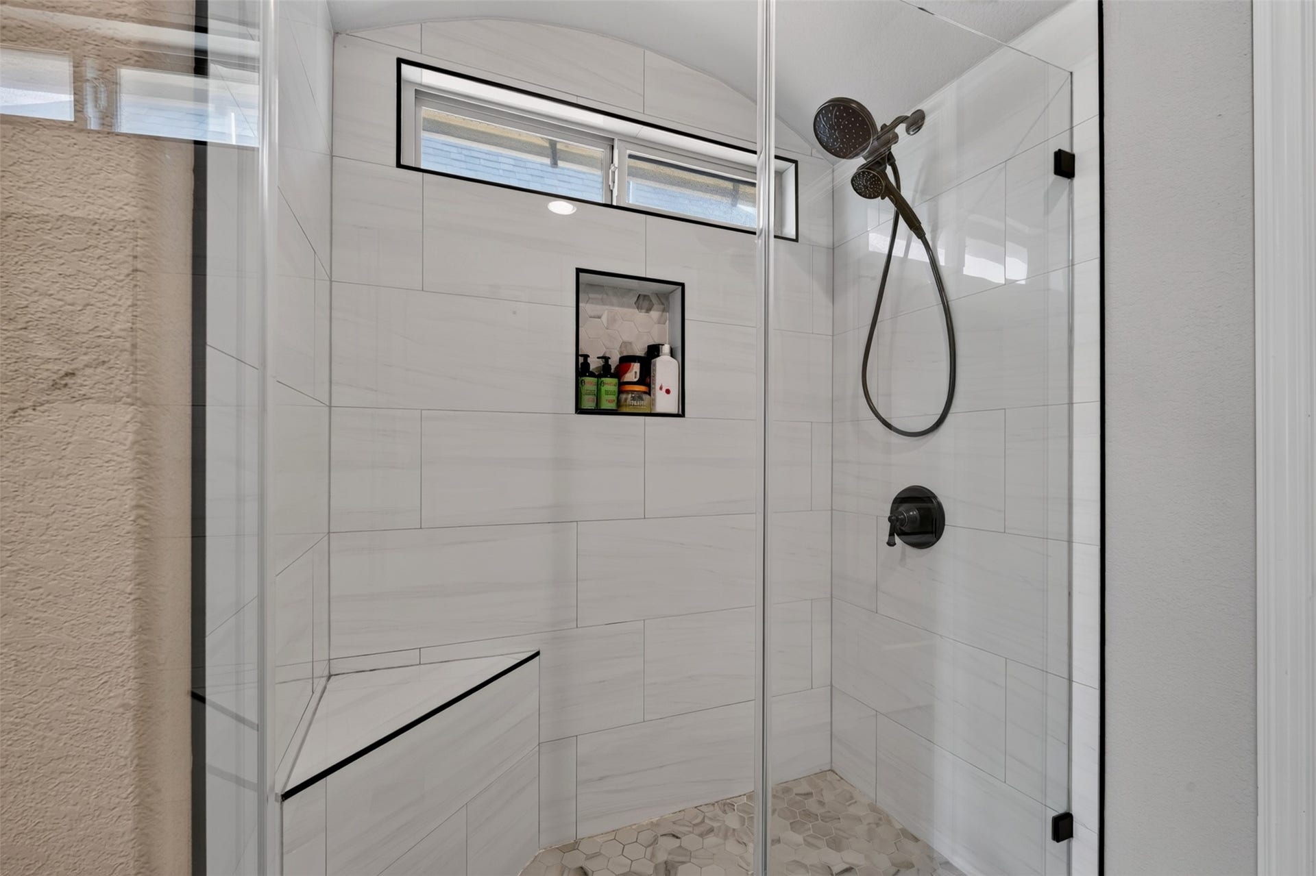 27818 Burchfield Grove Lane, Katy, TX 77494 Enjoy the modern look of this glass-enclosed walk-in shower, featuring large-format wall tile, a decorative niche, and dark fixtures. A built-in bench adds convenience while the high window allows natural light to brighten the space.