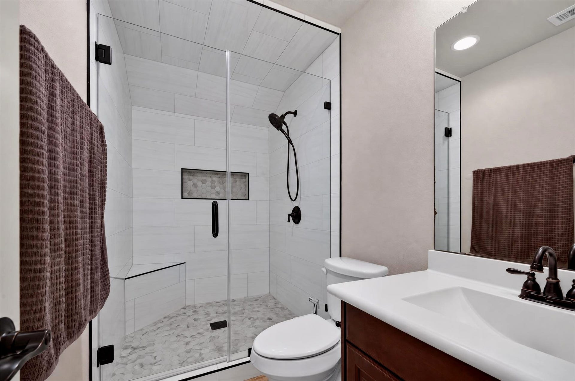 27818 Burchfield Grove Lane, Katy, TX 77494 The secondary bathroom showcases a glass-enclosed walk-in shower with crisp white wall tile, decorative mosaic flooring, and dark fixtures. A white countertop and warm wood cabinetry complete the clean, contemporary look.