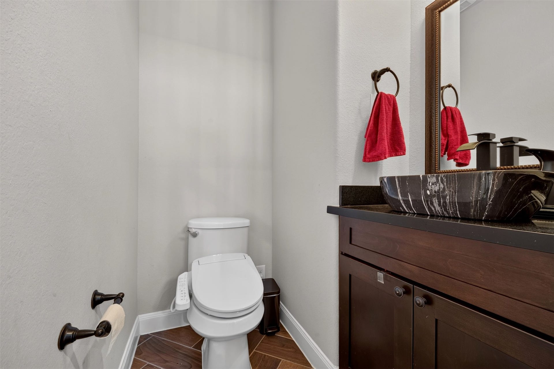 27818 Burchfield Grove Lane, Katy, TX 77494 A stylish vessel sink rests atop a dark countertop, paired with a rich wood vanity and a framed mirror. Warm wood-look flooring and coordinating fixtures give this conveniently located half bath a distinctive finish.