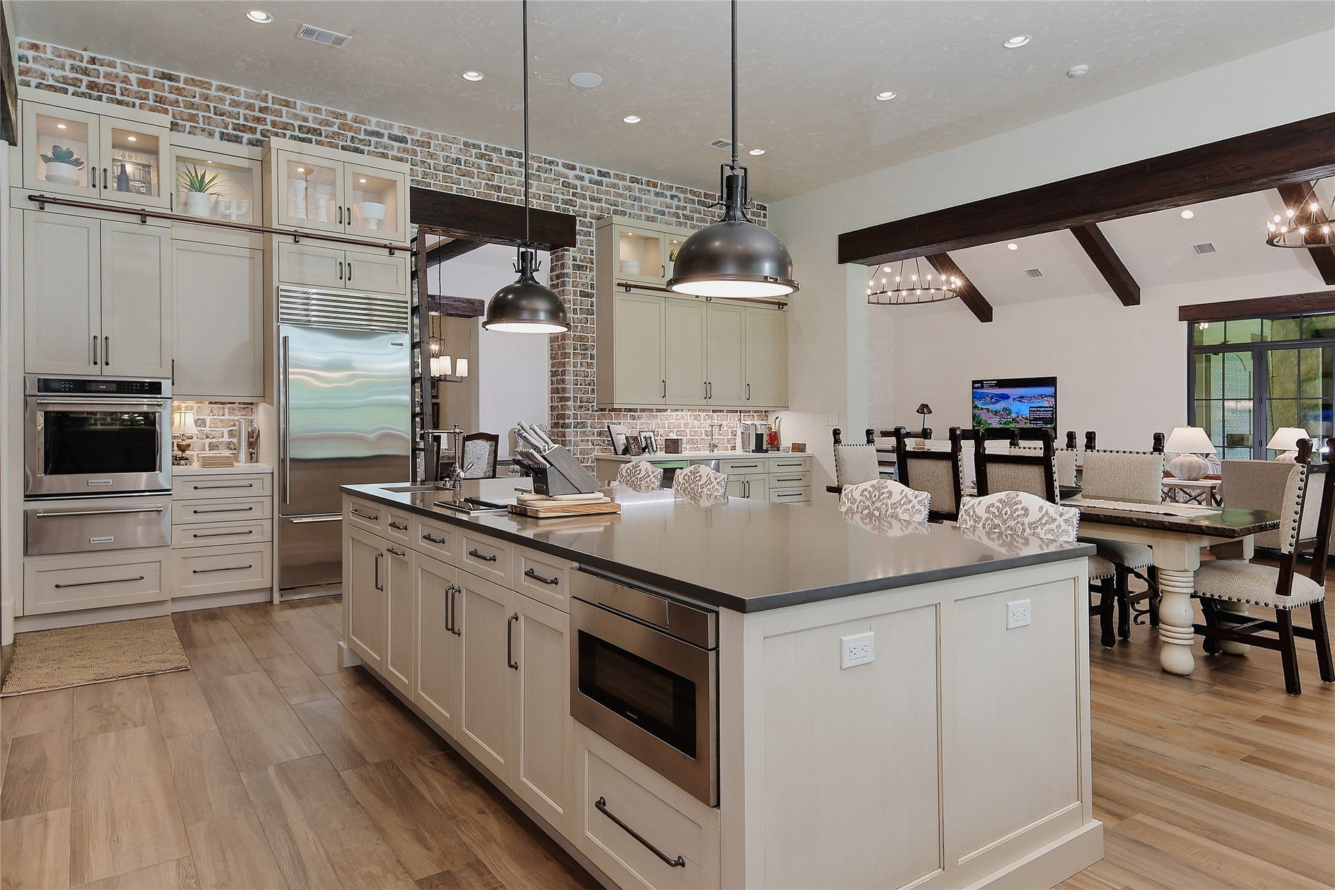 A Kitchen Aid wall oven, warming drawer and a steamer built into the island along with a drawer microwave, sink and disposal complete the appliance package. Pendant lighting and brick accents add a rustic elegance to the room.
