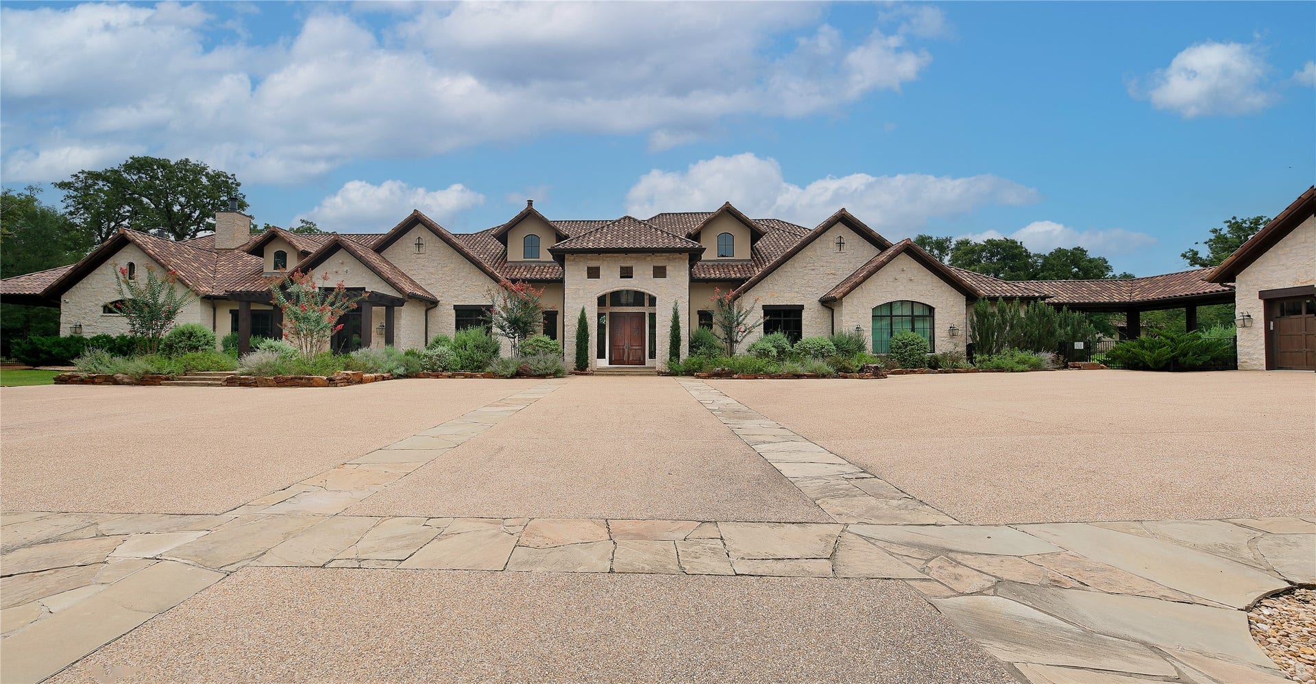 Dramatic architecture with a stone facade, multiple gables on the tiled roof & manicured landscaping.