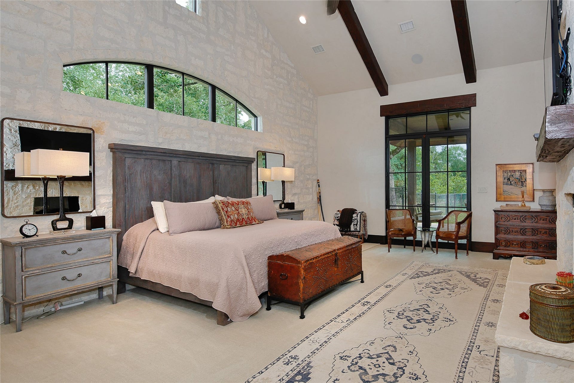 Unwind in this spectacular bedroom with plush carpeting, a stone double sided gas log fireplace, stone accent wall, vaulted ceiling, exposed beams and access to a private patio with yet another fireplace.