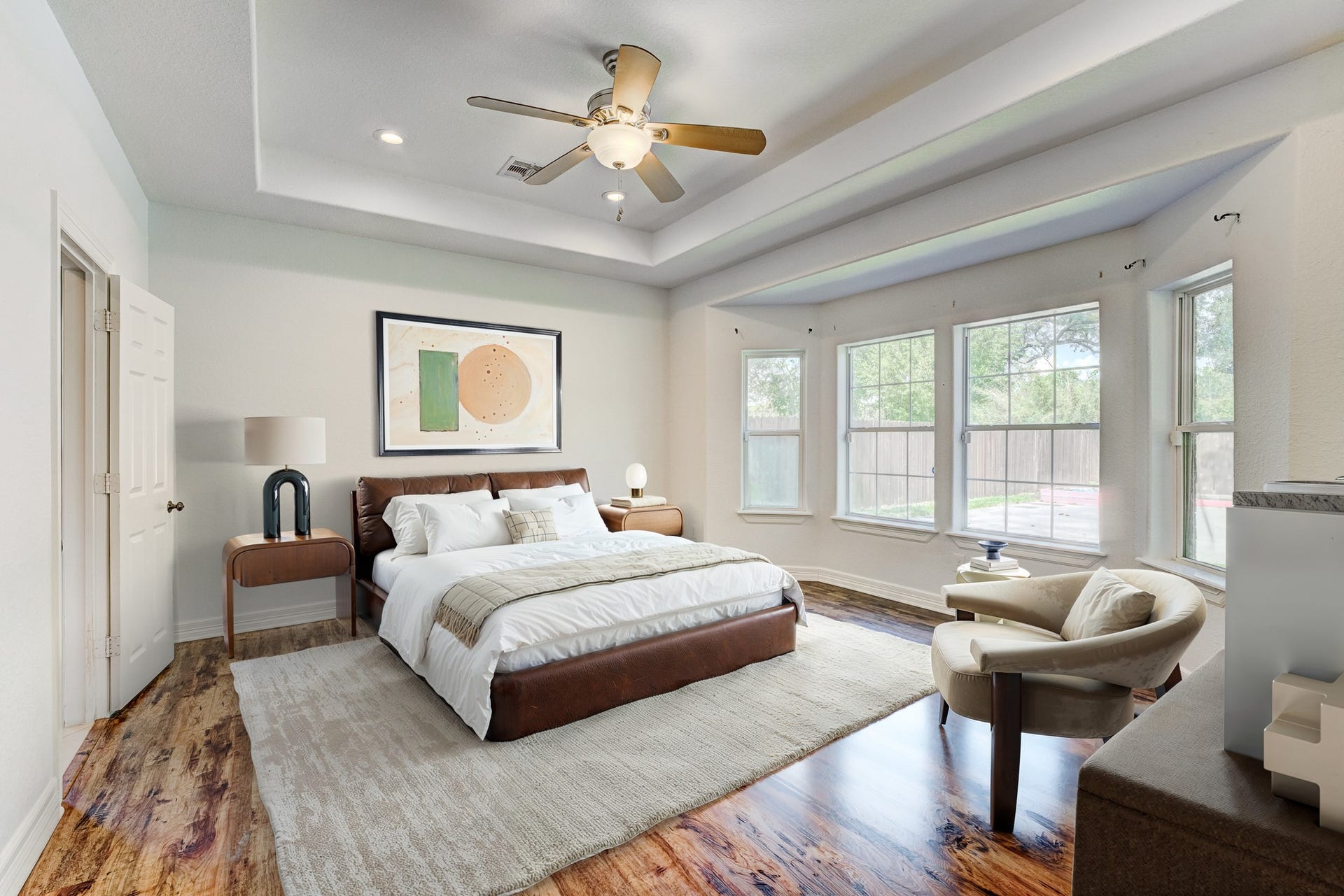 **Virtually Staged** Primary suite featuring tray ceiling, wood-look flooring, and oversized windows.