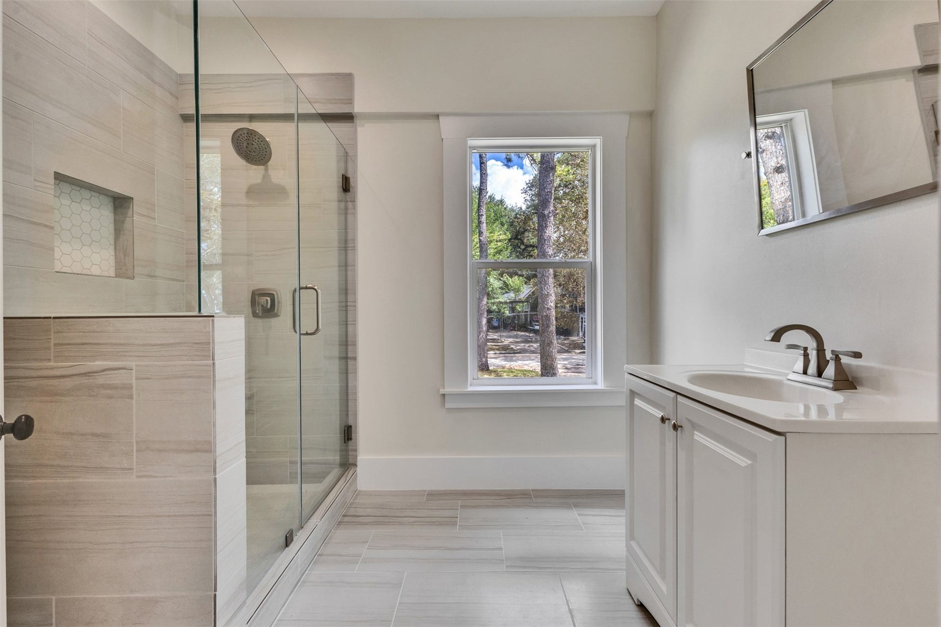 4534 Woodside Street, Houston, TX 77023 Modern bathroom featuring a spacious glass-enclosed shower, elegant tile work, and a bright window for natural light.
