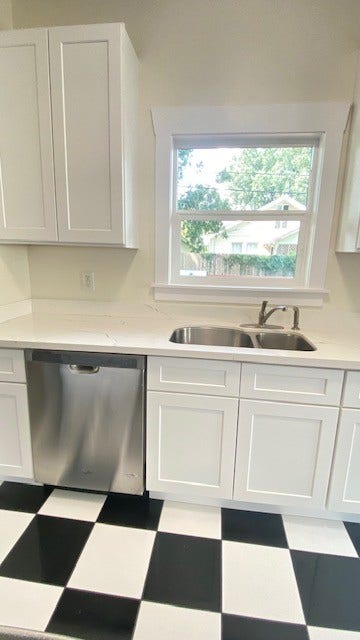 4534 Woodside Street, Houston, TX 77023 Bright kitchen featuring sleek white cabinets, a modern stainless steel dishwasher, and a charming black-and-white checkered floor.