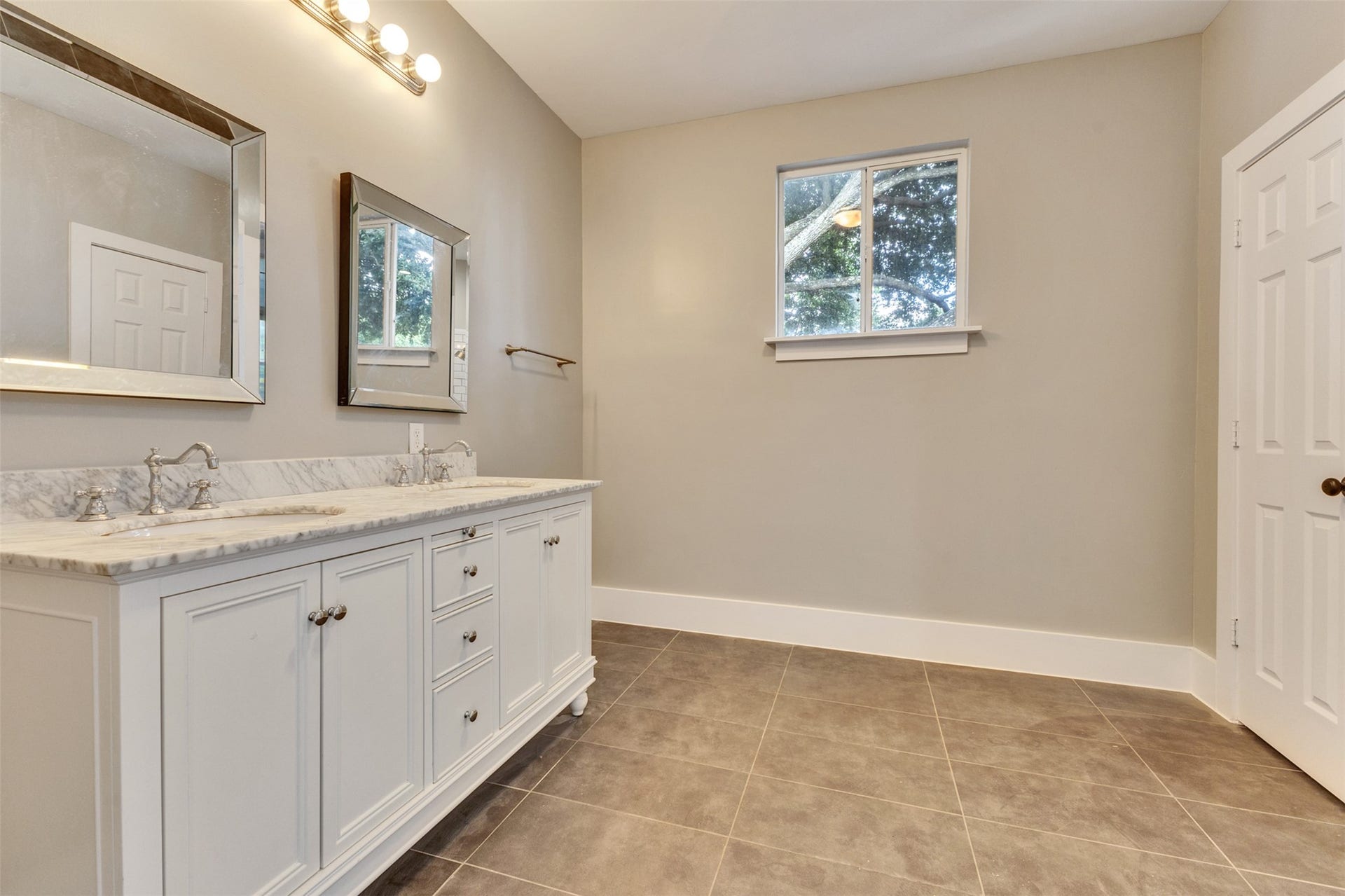 4534 Woodside Street, Houston, TX 77023 Spacious bathroom featuring a dual-sink vanity with elegant marble countertops, modern lighting, and a large mirror, complemented by neutral walls and stylish tile flooring.