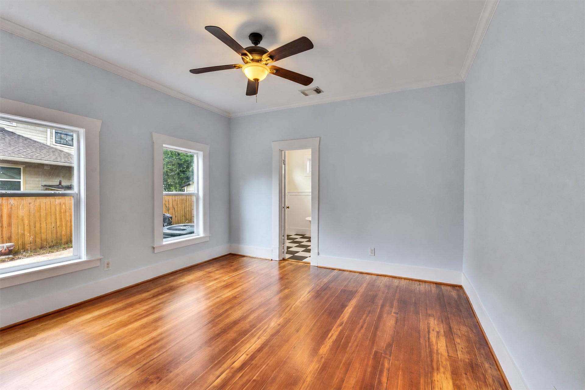 4534 Woodside Street, Houston, TX 77023 Spacious room with beautiful hardwood floors, abundant natural light from large windows, and a ceiling fan for comfort.