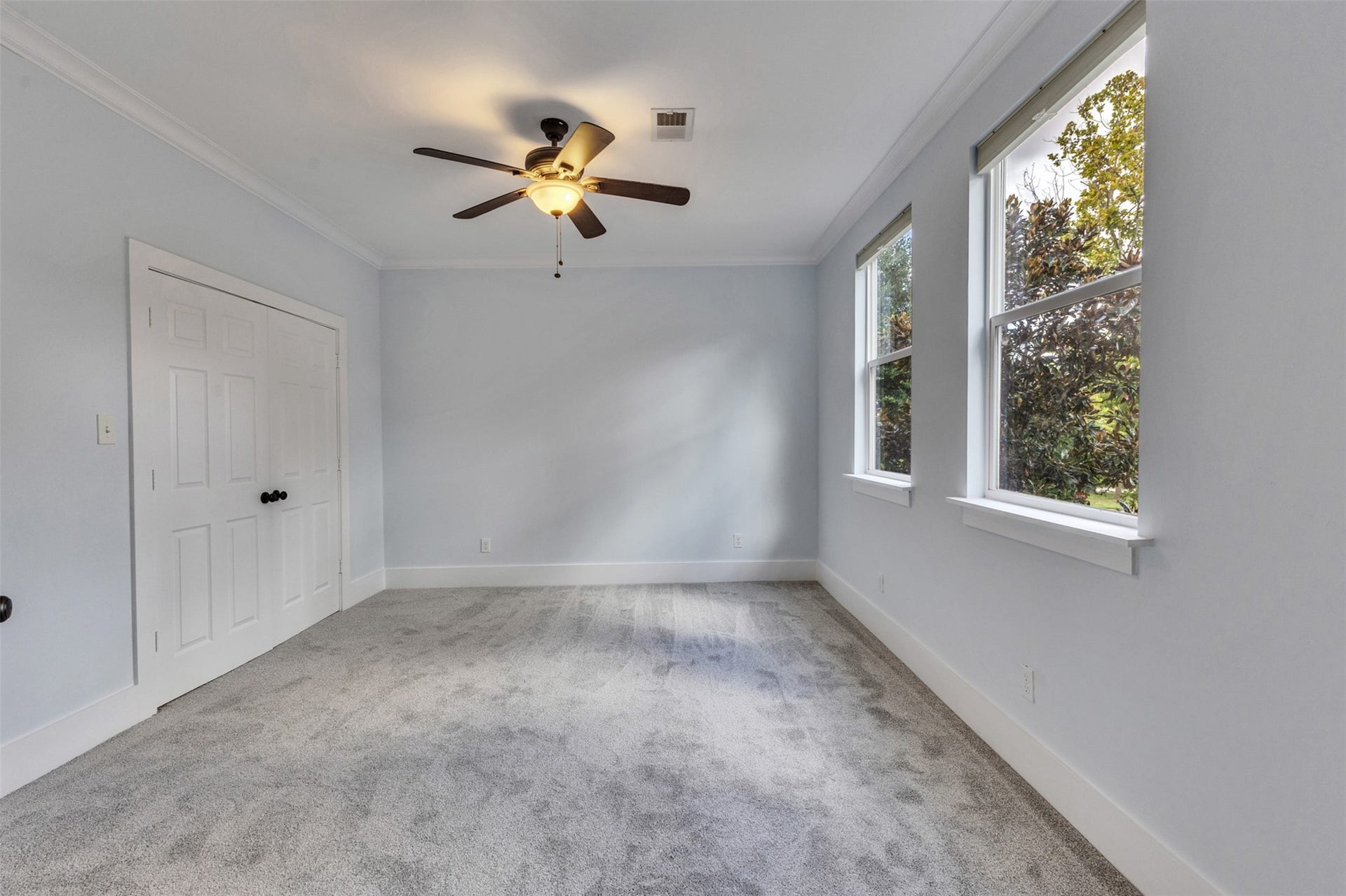 4534 Woodside Street, Houston, TX 77023 Bright and airy bedroom featuring soft carpet, a ceiling fan, and ample natural light from large windows, offering a serene and cozy space.