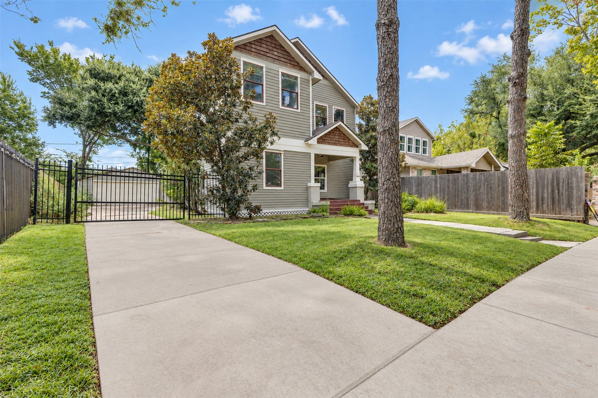 4534 Woodside Street, Houston, TX 77023 Charming two-story home with a welcoming front porch, nestled behind mature trees and featuring a gated driveway for added privacy.