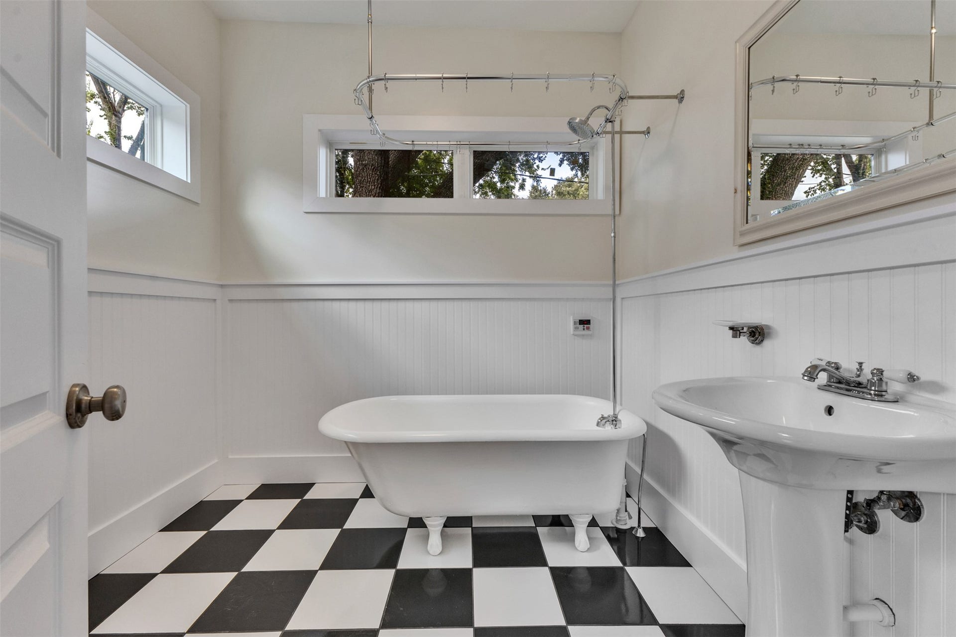4534 Woodside Street, Houston, TX 77023 Charming bathroom featuring a classic clawfoot tub, elegant pedestal sink, and stylish black and white checkered flooring, complemented by natural light through large windows.