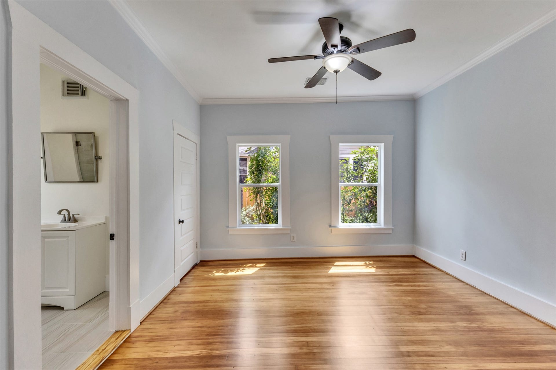 4534 Woodside Street, Houston, TX 77023 Bright and airy room featuring hardwood floors, large windows for natural light, and a ceiling fan, with an adjoining bathroom for convenience.