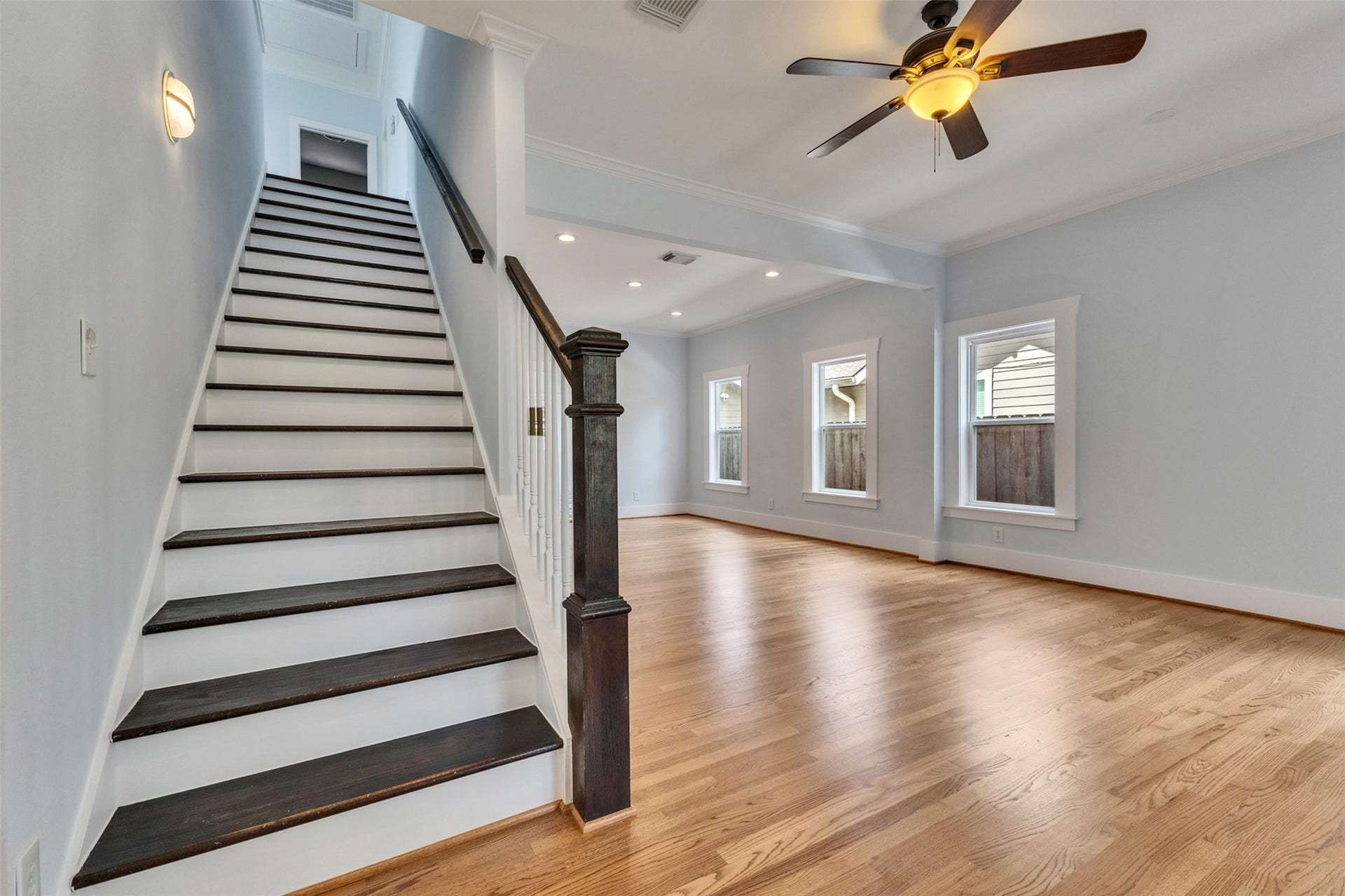 4534 Woodside Street, Houston, TX 77023 Spacious living area with gleaming hardwood floors and a ceiling fan, complemented by natural light from multiple windows. A classic staircase with dark wood accents adds elegance and leads to the upper level.