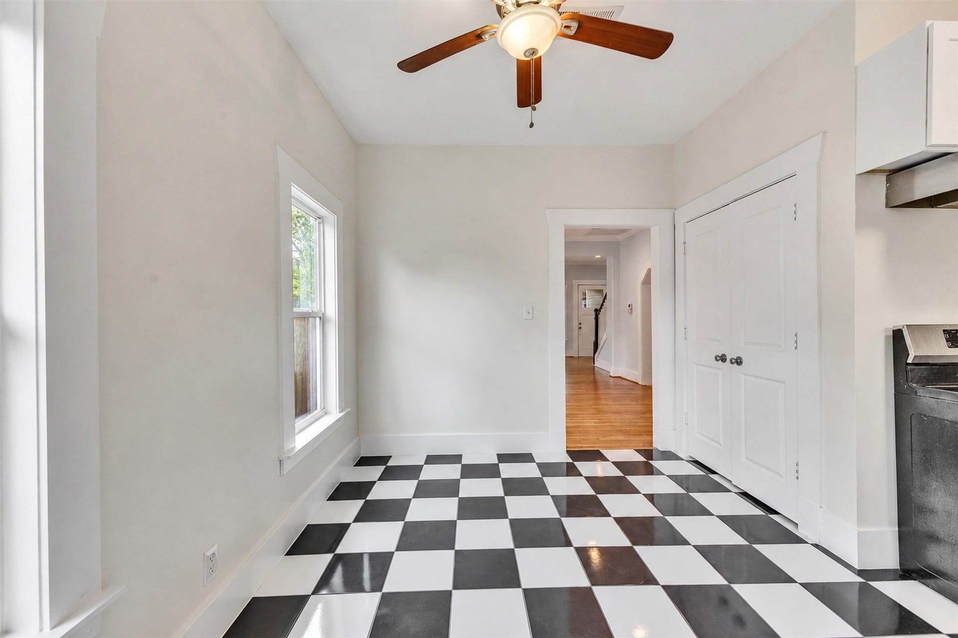 4534 Woodside Street, Houston, TX 77023 Bright and welcoming space featuring classic black-and-white checkered flooring, a ceiling fan, and ample natural light from a large window, perfect for a cozy dining area or breakfast nook.