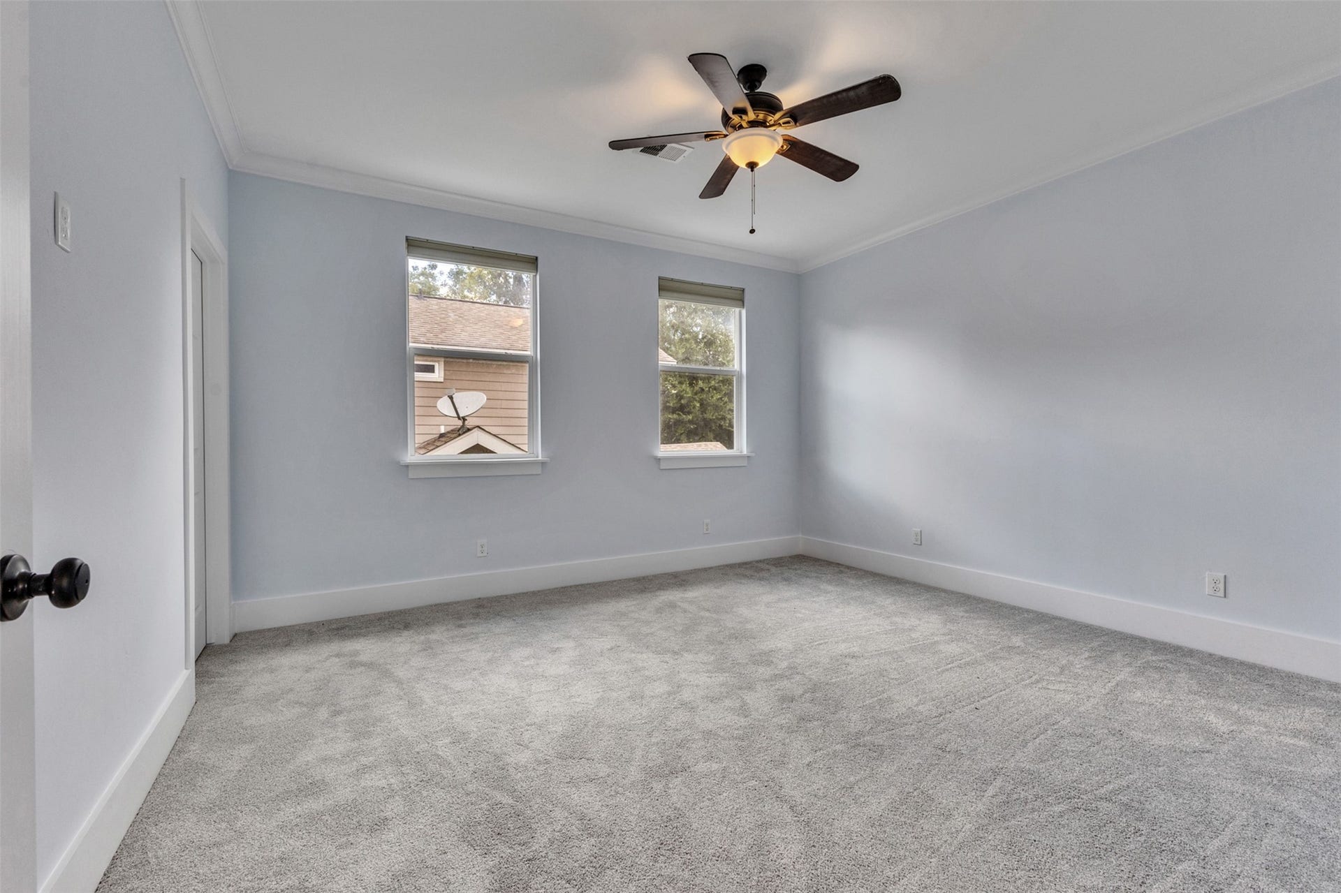 4534 Woodside Street, Houston, TX 77023 Spacious bedroom featuring soft gray carpeting and ample natural light from two large windows, complemented by a modern ceiling fan.