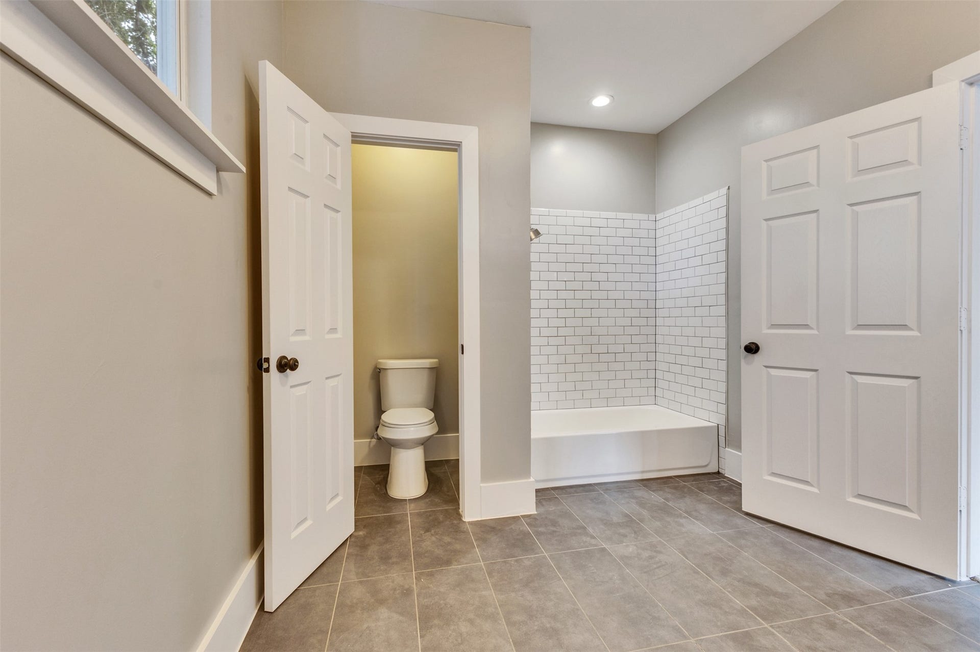 4534 Woodside Street, Houston, TX 77023 Spacious bathroom featuring sleek gray tile flooring, a classic subway-tiled shower, and a separate toilet area for added privacy.