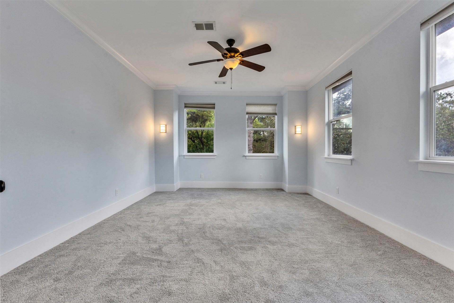 4534 Woodside Street, Houston, TX 77023 Spacious room with soft gray carpeting and ample natural light from multiple windows, featuring elegant wall sconces and a ceiling fan.
