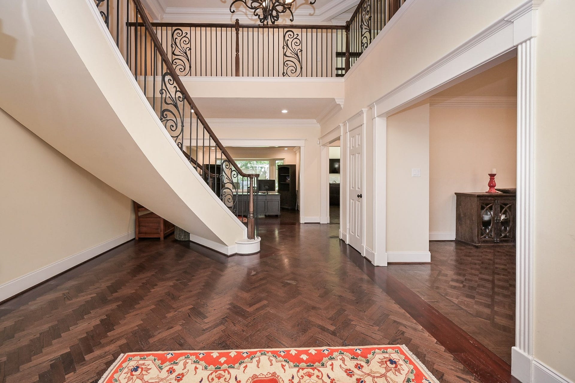 This photo showcases a spacious, elegant foyer with a grand staircase featuring ornate iron railings. The space has rich hardwood floors and high ceilings, offering a welcoming entryway.