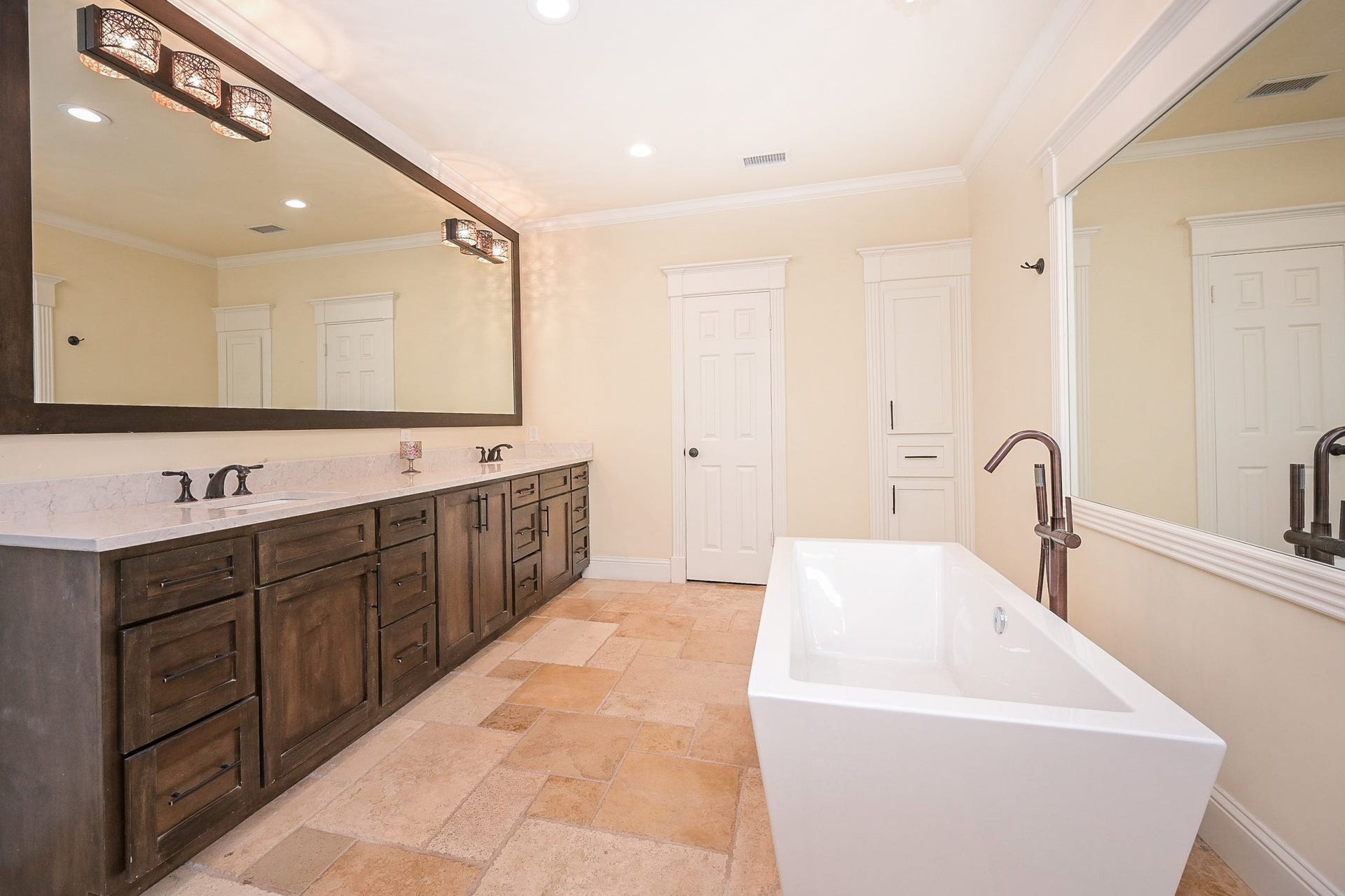 The dual sinks and a long vanity provide ample cabinet storage. It has elegant lighting, expansive mirrors, and a neutral color palette, offering a clean and stylish atmosphere.