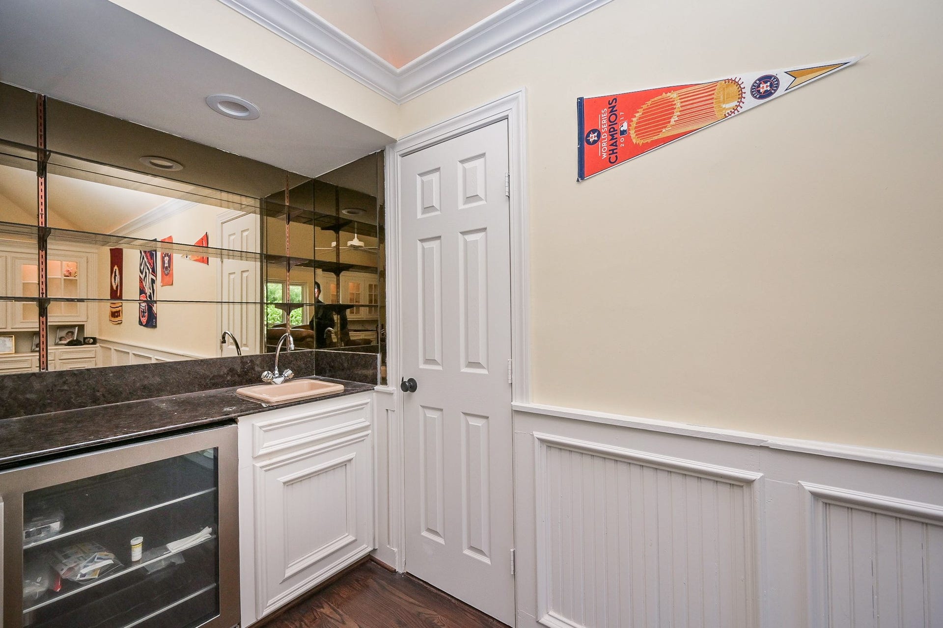 In the game room is also a wet bar area with a sink, dark countertop, and mirrored backsplash. There's a mini fridge and cabinetry below as well as a storage closet through the door on the right.