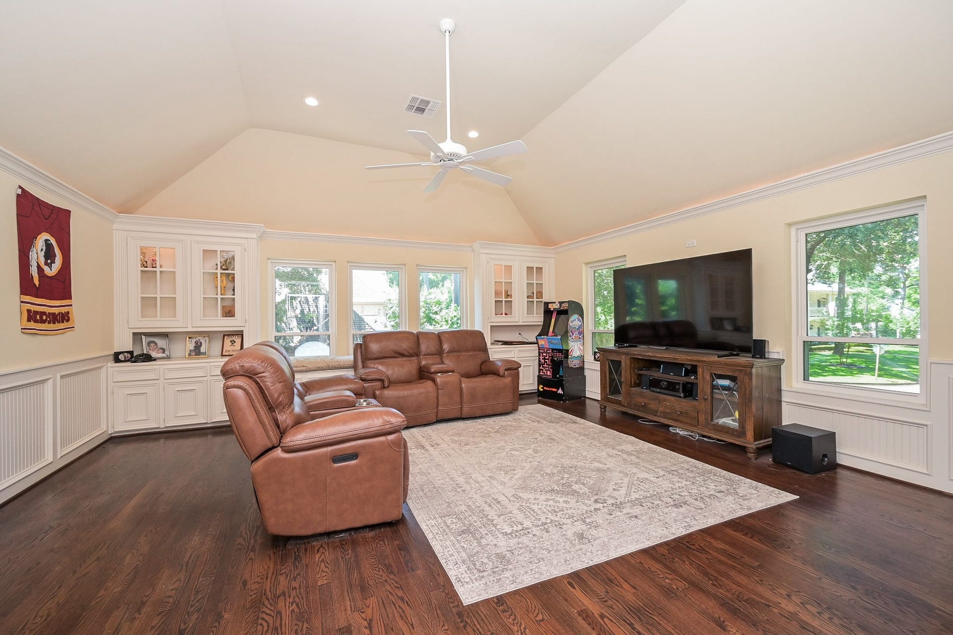 Upstairs, this spacious game room features hardwood floors, a vaulted ceiling, and large windows that provide ample natural light. It includes built-in cabinetry and a window seat.