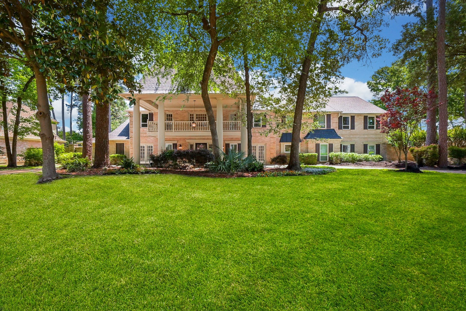 This charming two-story home features a classic brick exterior, elegant balcony, and large windows. Nestled among mature trees, it boasts a spacious, well-manicured front lawn, perfect for outdoor activities and entertaining.