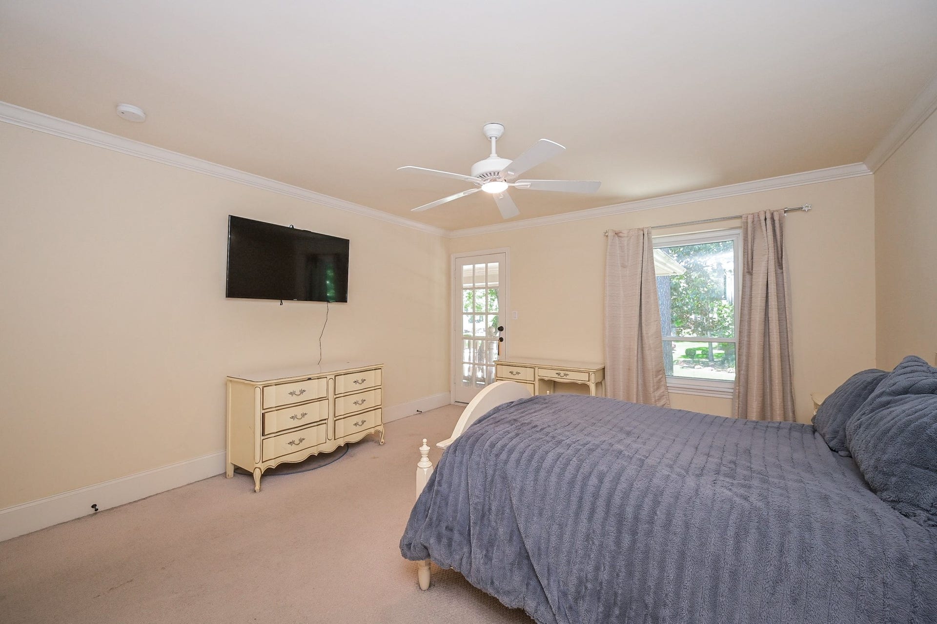 Spacious bedroom with natural light, featuring a window and glass door access to the balcony. Neutral walls and carpet create a cozy atmosphere. There is also direct access to a hollywood bath.