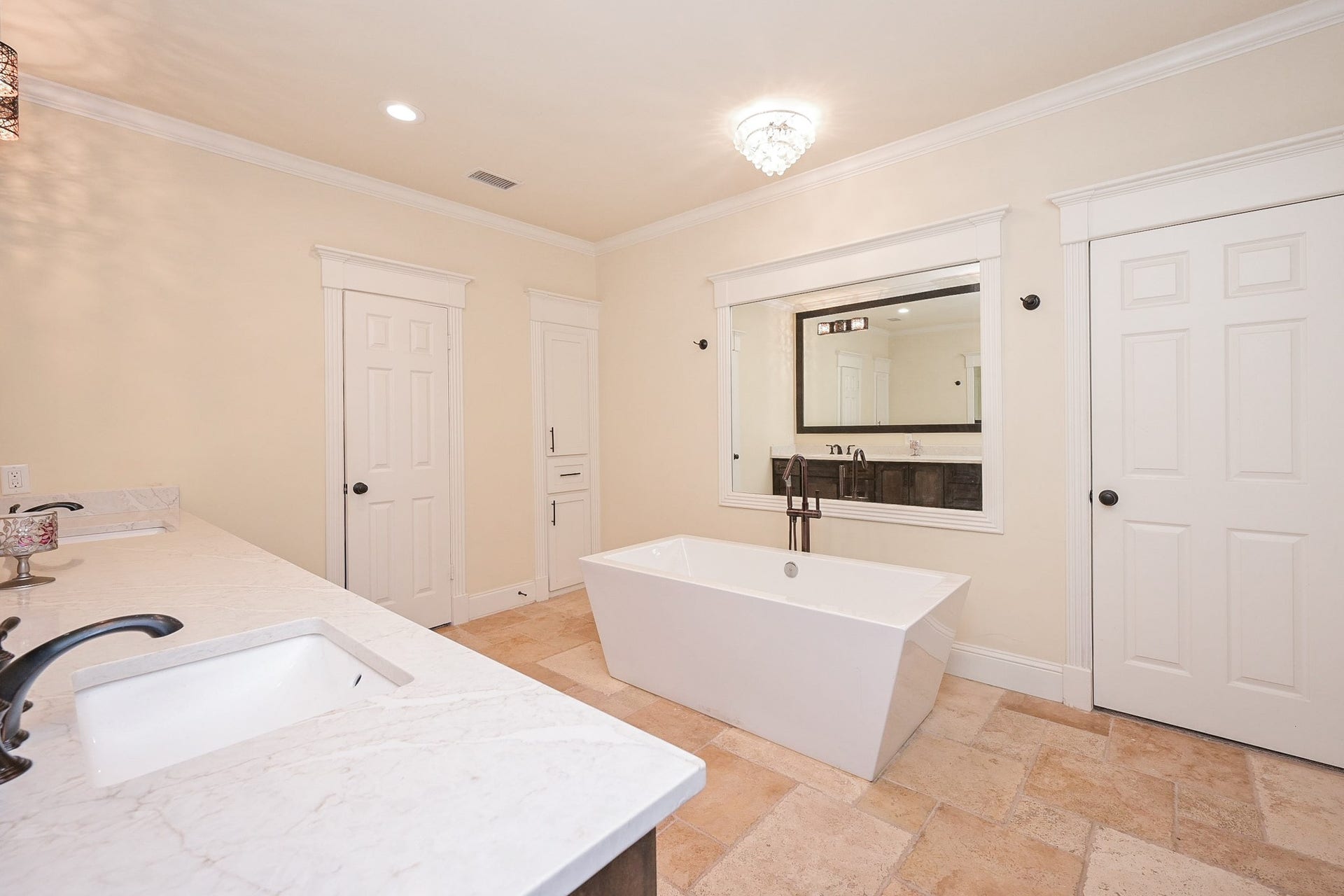 This primary bathroom features a modern freestanding tub, a spacious quartz countertop with dual sinks, and access to 2 walk in closets. The neutral color palette and recessed lighting create a calming, luxurious atmosphere.