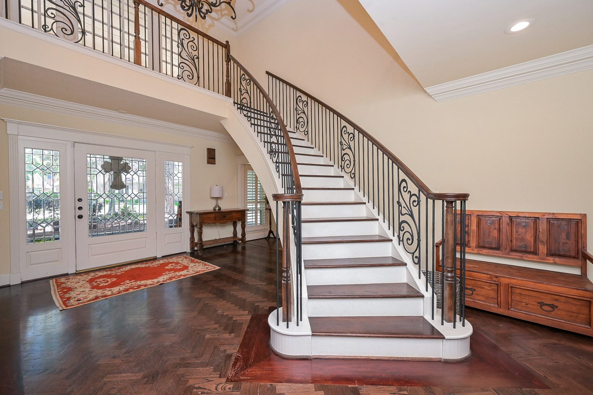 This elegant entryway features a grand curved staircase with ornate iron railings, dark hardwood floors, and a large windowed front door.