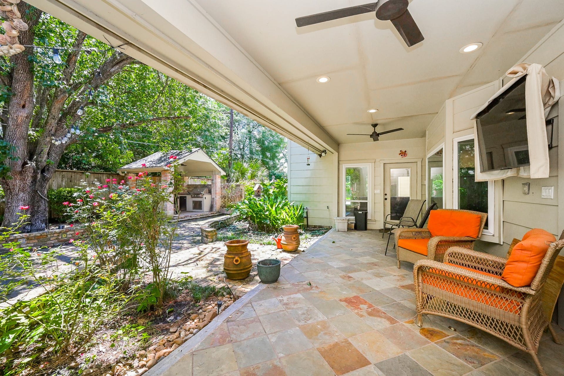This inviting outdoor space features a covered patio with ceiling fans and access from the primary bedroom, sitting room and living room. It overlooks a beautifully landscaped backyard with mature trees and a built-in outdoor kitchen, perfect for entertaining.