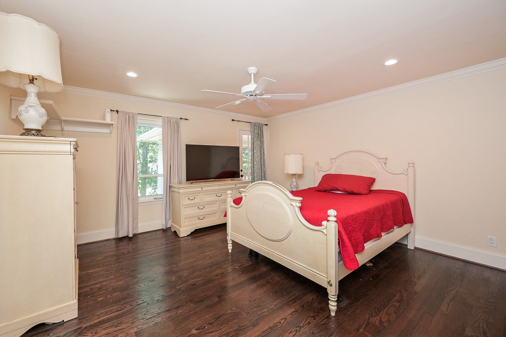 This bedroom features elegant hardwood floors and access to the second story front balcony. Large windows allow natural light, complemented by recessed lighting and a ceiling fan for comfort.