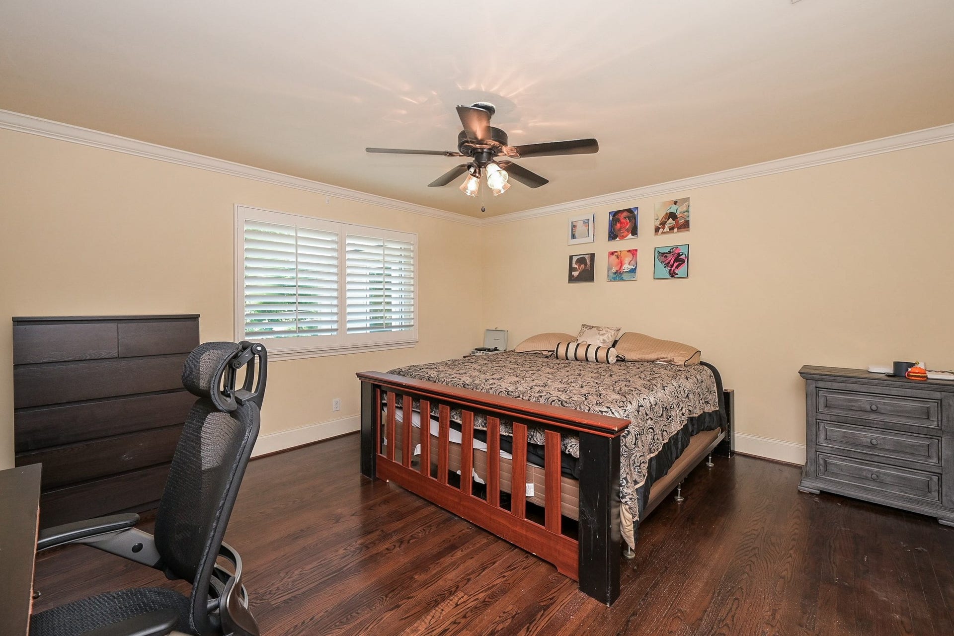 This spacious bedroom features hardwood floors and a ceiling fan. It includes a window with shutters for natural light and a cozy atmosphere. There is also direct access to a hollywood bath.