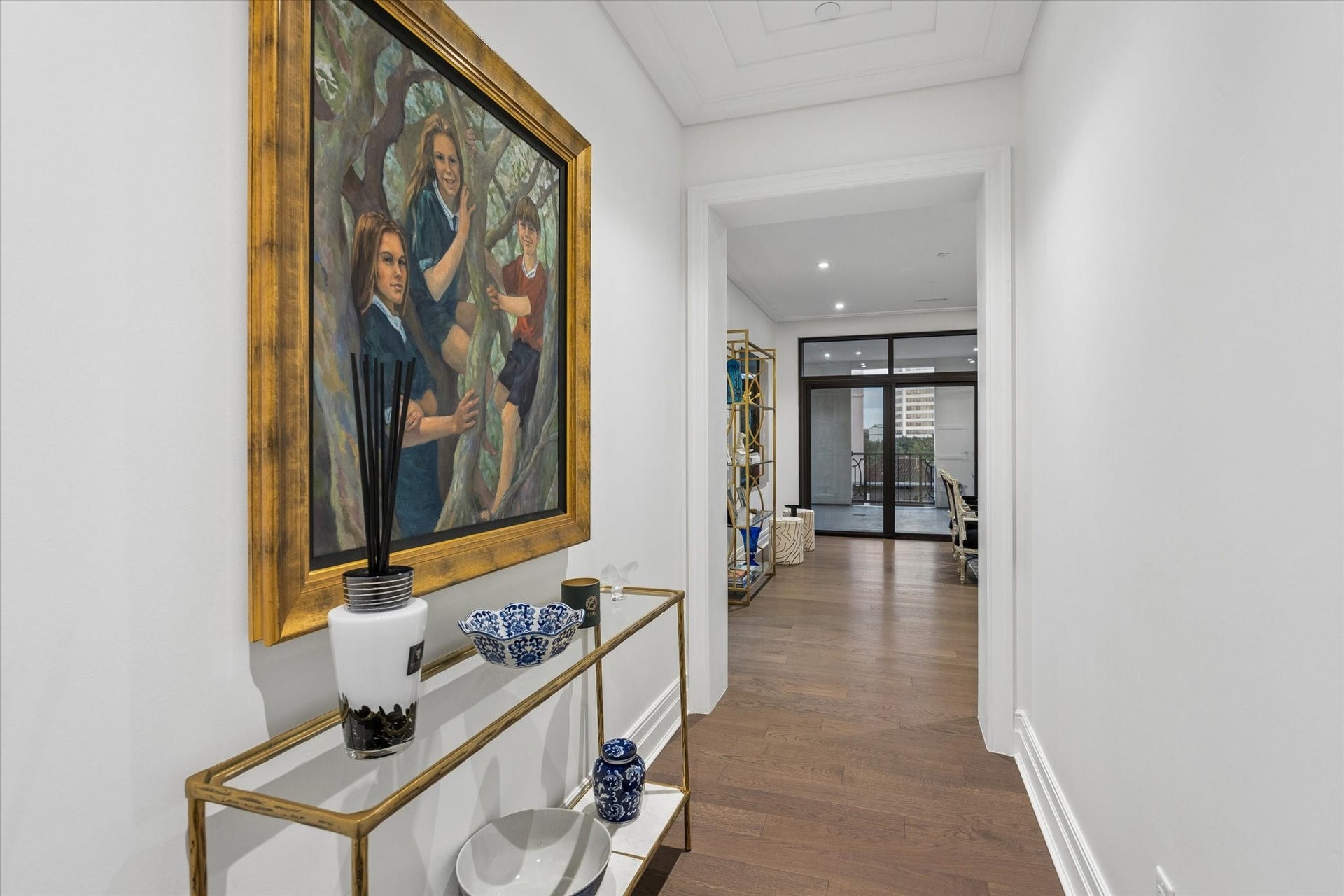 6017 Memorial Drive, #505, Houston, TX 77007 A gracious entry hallway creates an elegant sense of arrival, drawing the eye through the residence toward the light-filled living spaces and expansive glass doors beyond. Rich Listone Giordano engineered hardwood flooring provides visual continuity, while crisp white walls, refined architectural detailing, and gallery-style artwork enhance the clean European aesthetic. The uninterrupted sightline creates a beautiful sense of depth, openness, and effortless flow.